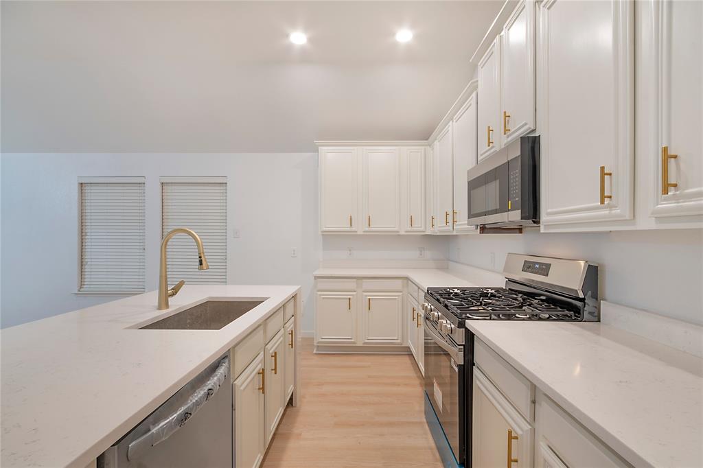 549 Hickory Lane Fate, TX 75087 - Photo 9 of 38 Kitchen with stainless steel appliances, light wood-style floors, light stone counters, and white cabinetry