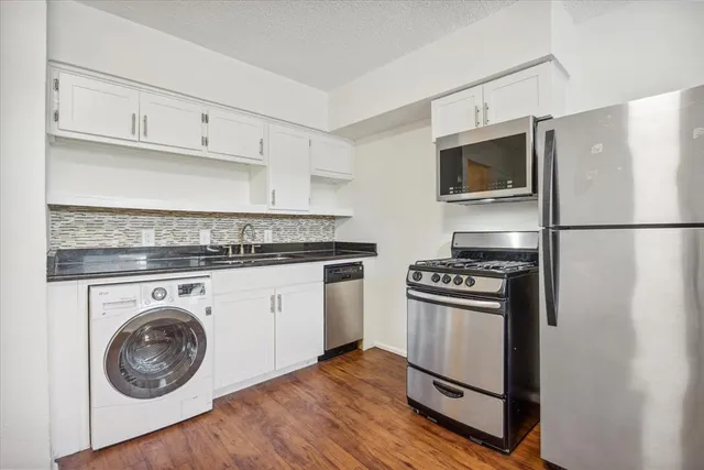 a kitchen with white cabinets stainless steel appliances and wooden floor