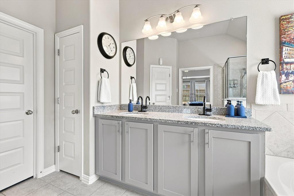 15729 Preble Road Fort Worth, TX 76177 - Photo 20 of 37 Spacious Primary Bath features a Vaulted Ceiling, Dual-sink Granite Mirrored Vanity, Abundant Cabinetry, Tile Flooring. A Deep Soaking Tub with Tiled Surround Complemented by a Separate Tiled Walk-in Shower with Frameless Glass Enclosure and Built-in Corner Shelves. There's also Convenient Access to the Linen and Walk-in Closets.