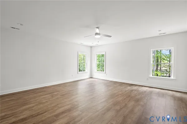 an empty room with wooden floor chandelier fan and windows