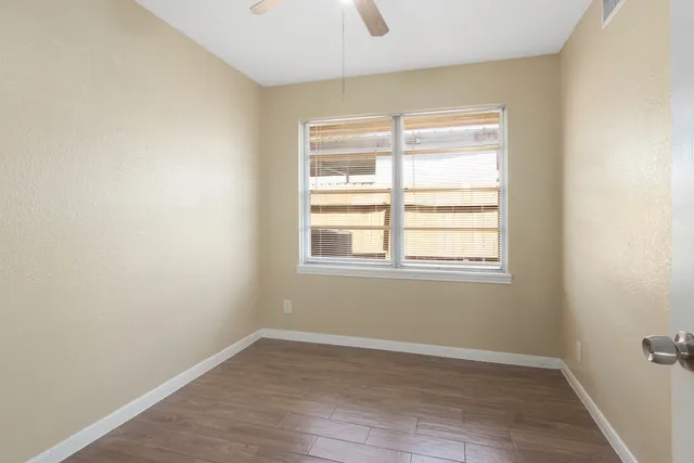 a view of an empty room with wooden floor and a window
