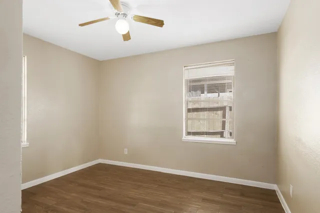 an empty room with wooden floor chandelier fan and windows