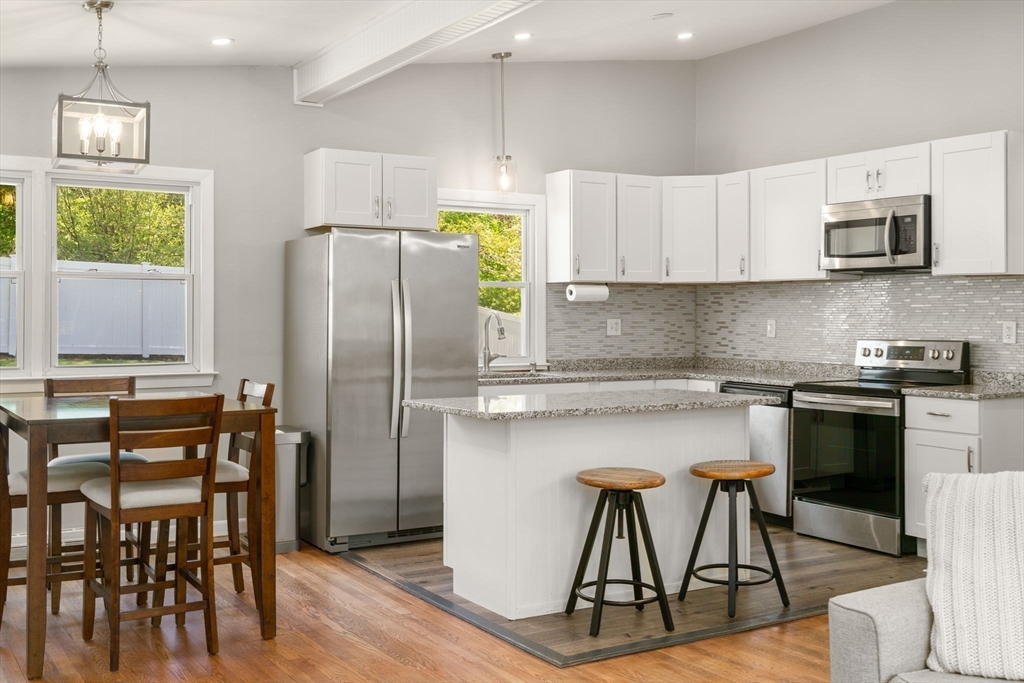 6 Rosenfeld Road Millis, MA 02054 - Photo 2 of 23 a kitchen with stainless steel appliances granite countertop a stove a refrigerator a microwave a dining table and chairs with wooden floor