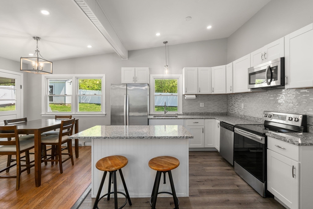 6 Rosenfeld Road Millis, MA 02054 - Photo 3 of 23 a kitchen with stainless steel appliances granite countertop a stove top oven a sink a dining table and chairs with wooden floor