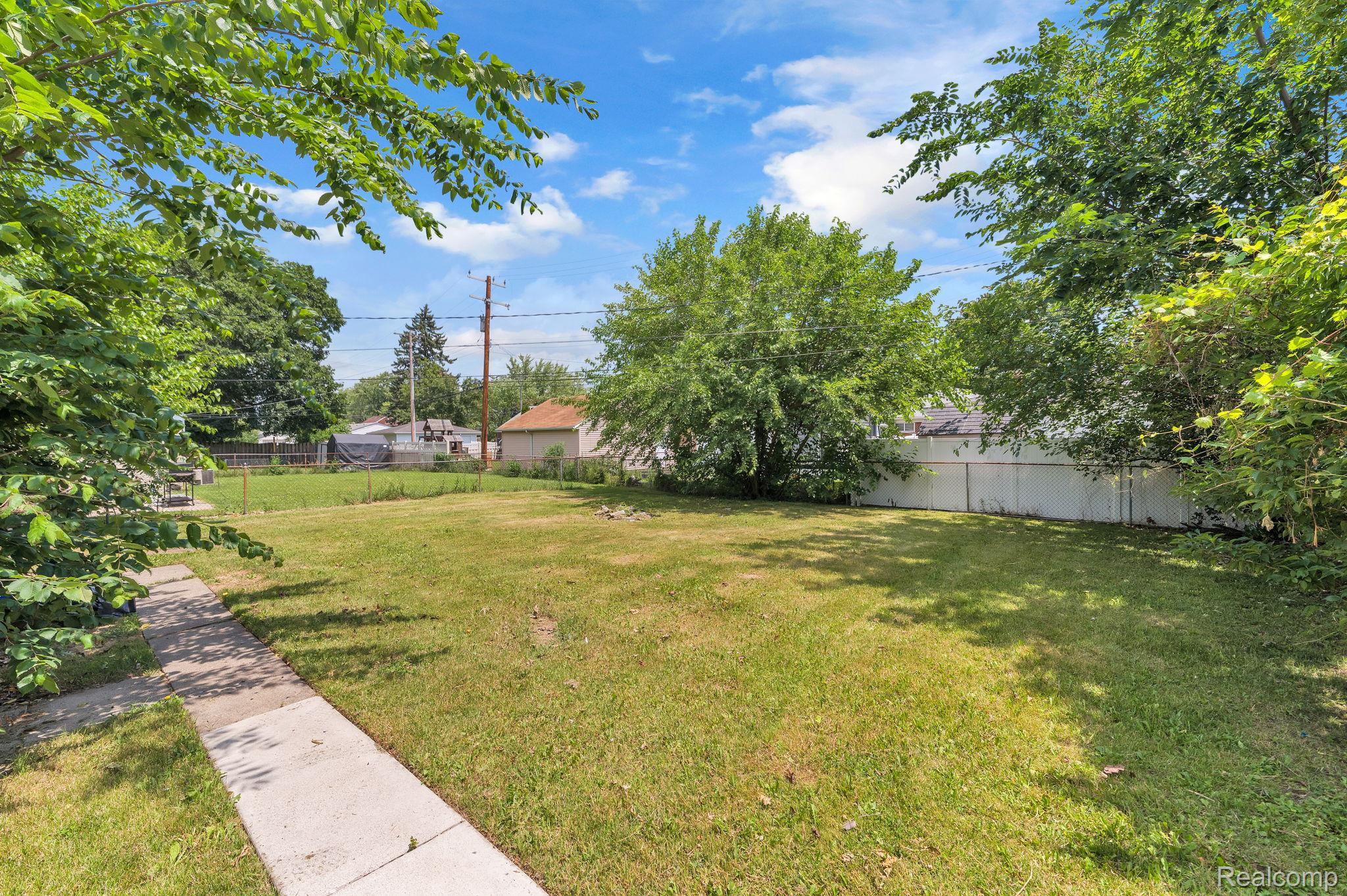 7641 Pelham Road Allen Park, MI 48101 - Photo 5 of 21 Expansive lot featuring a large grassy area, mature perimeter trees, a concrete walkway, and partial fencing