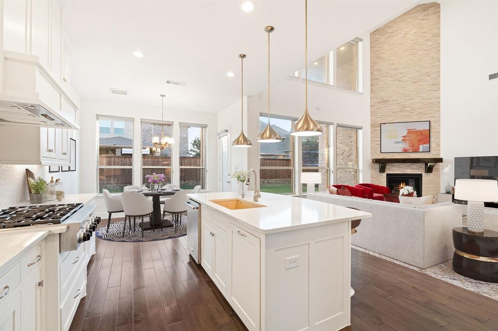 2441 Flat Creek Road Frisco, TX 75036 - Photo 34 of 34 Kitchen featuring white cabinetry, a stone fireplace, decorative light fixtures, open floor plan, and an island with sink