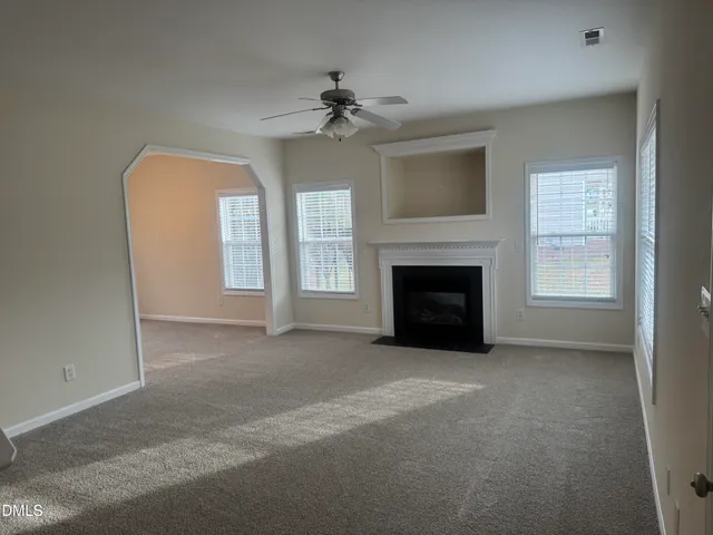 an empty room with windows fireplace and fan