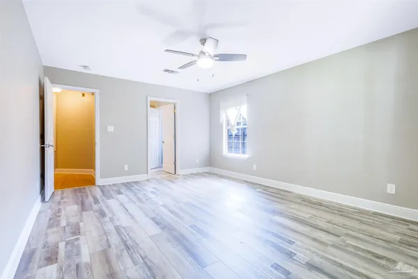 an empty room with wooden floor chandelier fan and windows