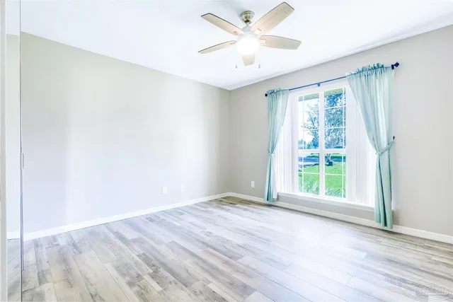 an empty room with wooden floor fan and windows