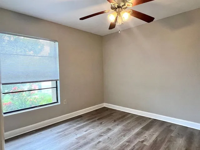 an empty room with wooden floor fan and windows