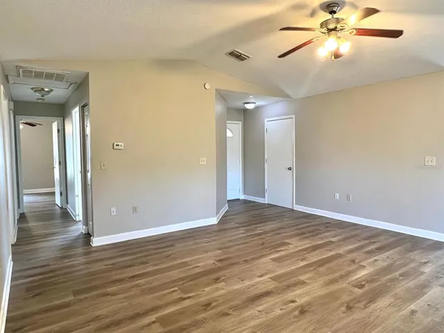 a view of an empty room with wooden floor and a ceiling fan