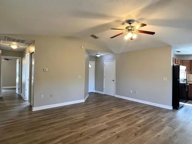 a view of an empty room with wooden floor and a ceiling fan