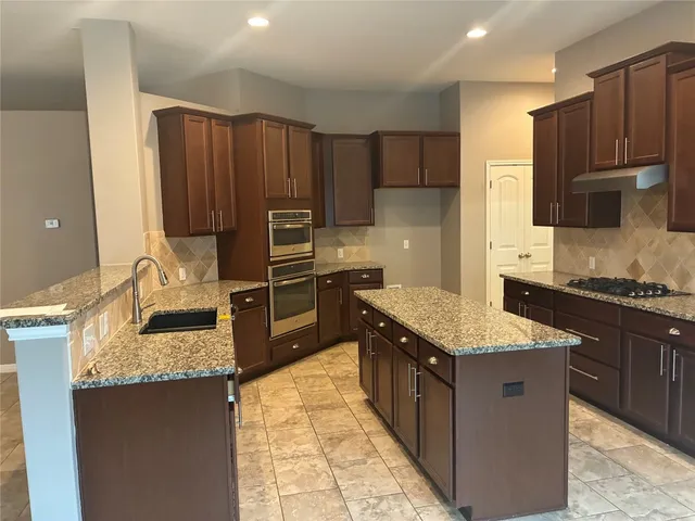 a kitchen with kitchen island granite countertop stainless steel appliances and wooden cabinets