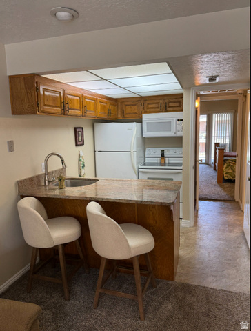 860 South Village Road, Unit Z10 St. George, UT 84770 - Photo 4 of 18 Kitchen featuring a breakfast bar, a peninsula, wood finish cabinetry, white appliances, and light colored carpet