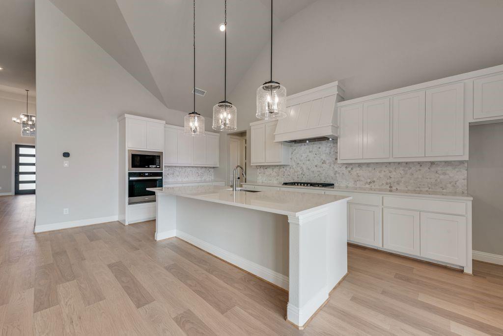1259 Calebria Way Fate, TX 75087 - Photo 7 of 38 a large kitchen with cabinets wooden floor stainless steel appliances and a fireplace