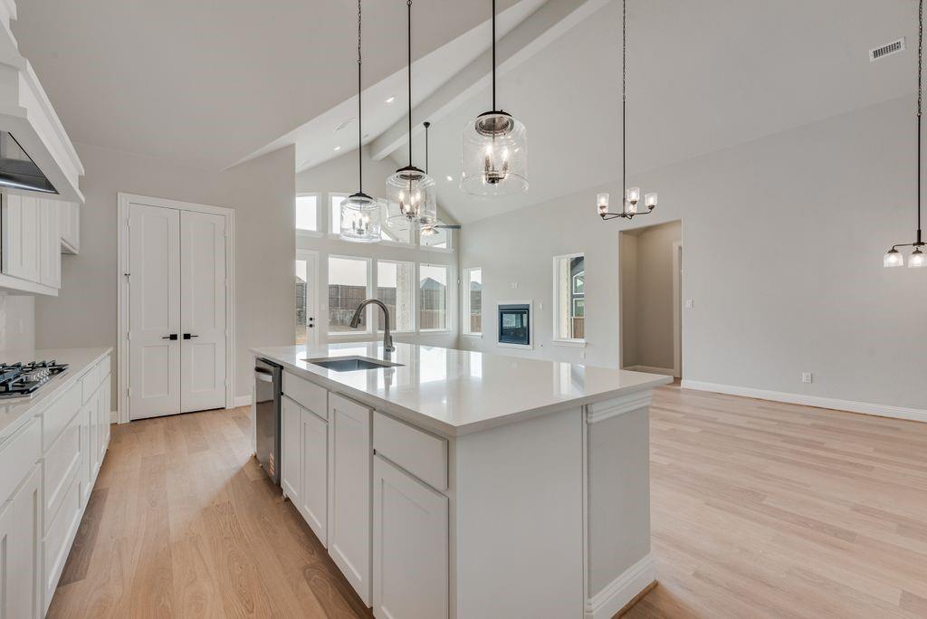 1259 Calebria Way Fate, TX 75087 - Photo 10 of 38 a large kitchen with kitchen island white cabinets and wooden floor