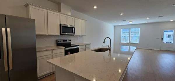 a kitchen with stainless steel appliances granite countertop a sink a microwave a refrigerator a stove and white cabinets with wooden floor