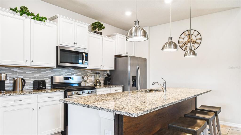 7219 Oakmoss Loop Davenport, FL 33837 - Photo 6 of 54 a kitchen with stainless steel appliances granite countertop a sink dishwasher a microwave oven a refrigerator with white cabinets and wooden floor
