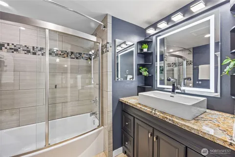 a bathroom with a granite countertop sink a mirror a bathtub and shower