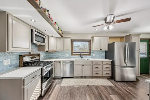 a kitchen with stainless steel appliances a stove a sink dishwasher a refrigerator white cabinets and wooden floor