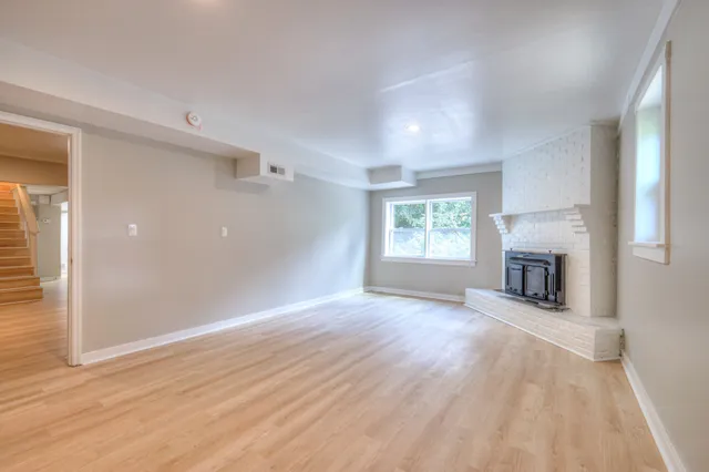 an empty room with wooden floor fireplace and windows