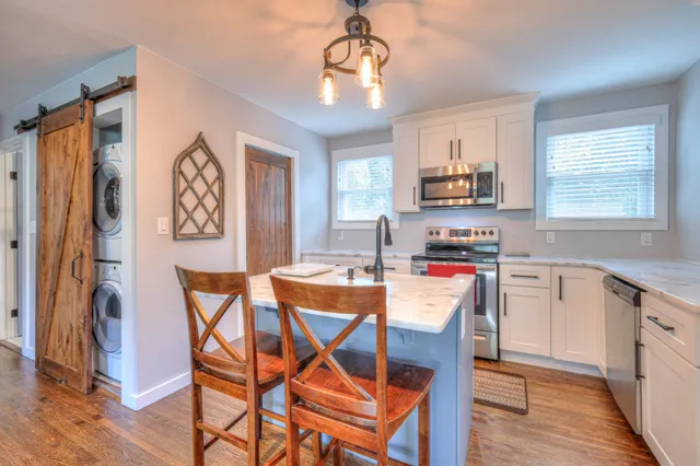 a kitchen with stainless steel appliances granite countertop a stove a refrigerator a sink dishwasher a dining table and chairs with wooden floor