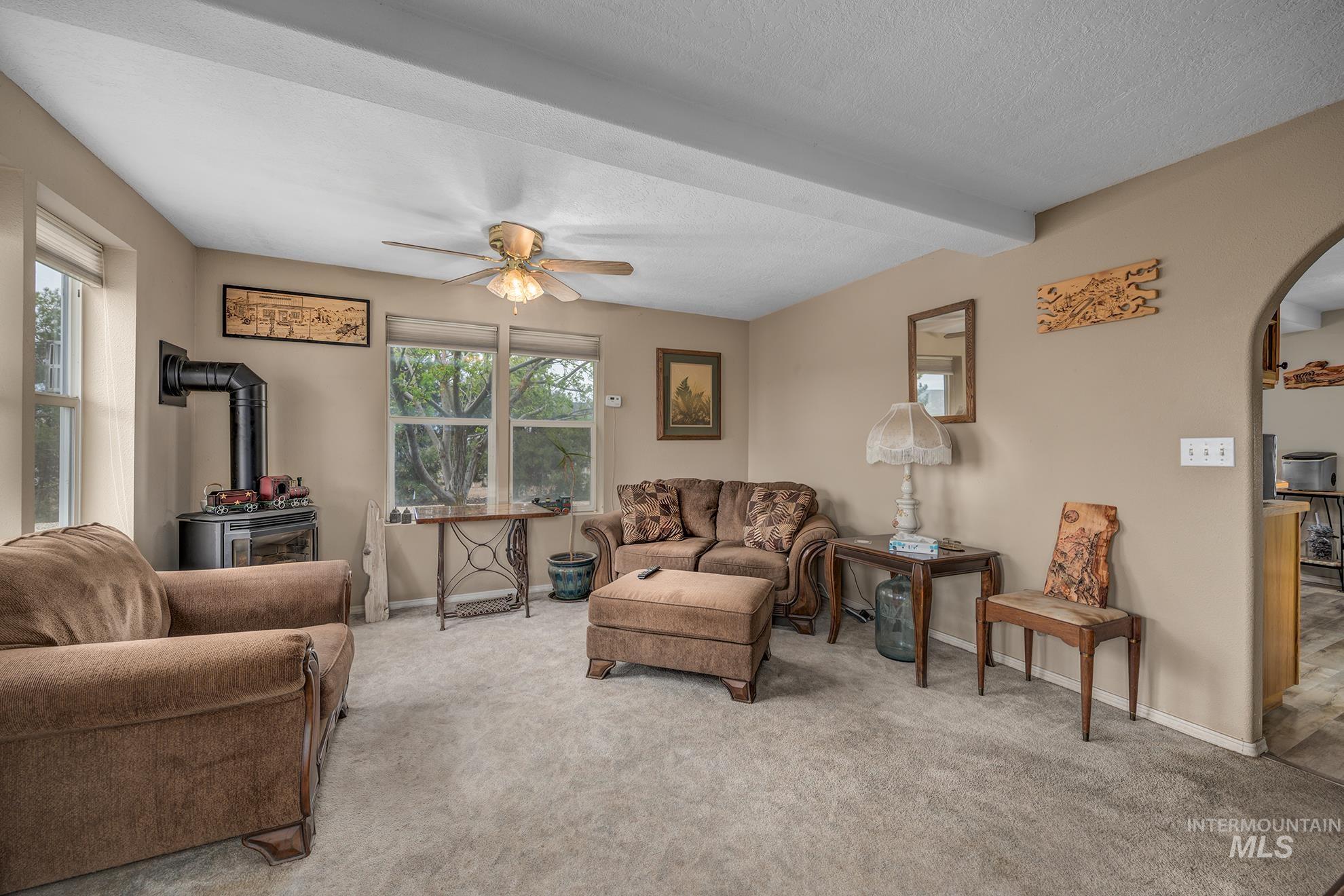 1363 Ross Road Weiser, ID 83672 - Photo 5 of 47 Carpeted living room with a wood stove, arched walkways, a ceiling fan, beam ceiling, and a textured ceiling