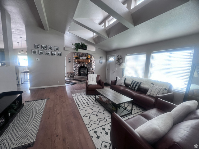 Spacious living area featuring vaulted ceilings with exposed beams, wood-finish flooring, and multiple windows