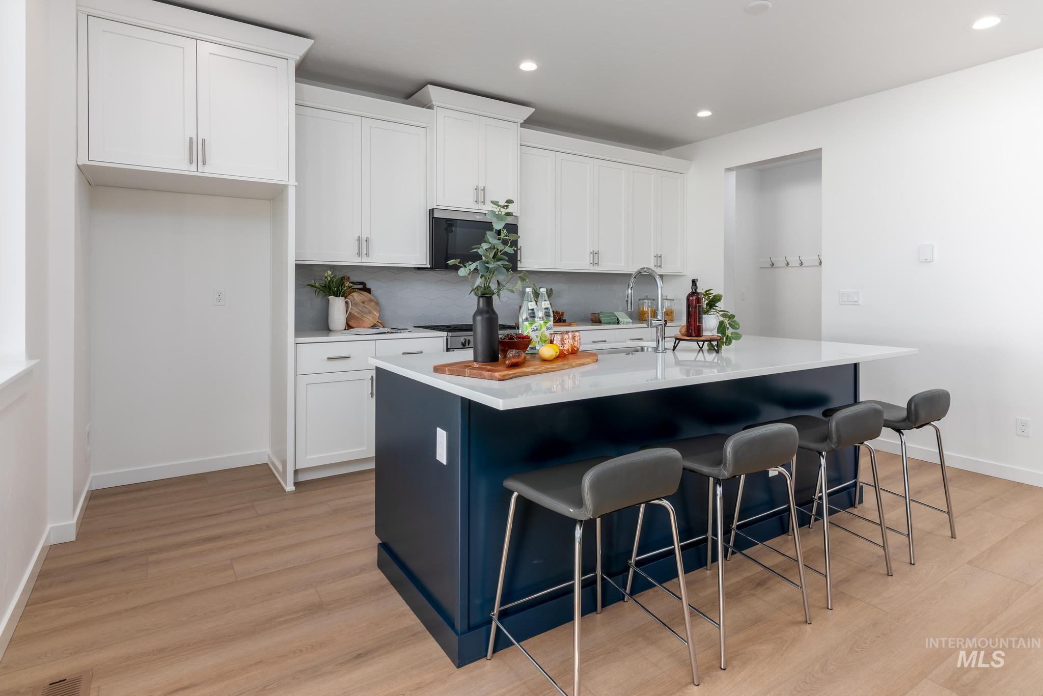 14566 Boatwatch Drive Caldwell, ID 83607 - Photo 10 of 42 Kitchen featuring white cabinetry, a center island with sink, a kitchen breakfast bar, tasteful backsplash, and light wood-type flooring