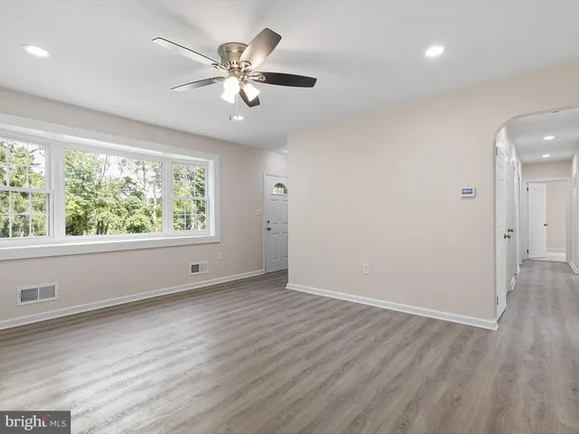 an empty room with wooden floor chandelier fan and windows