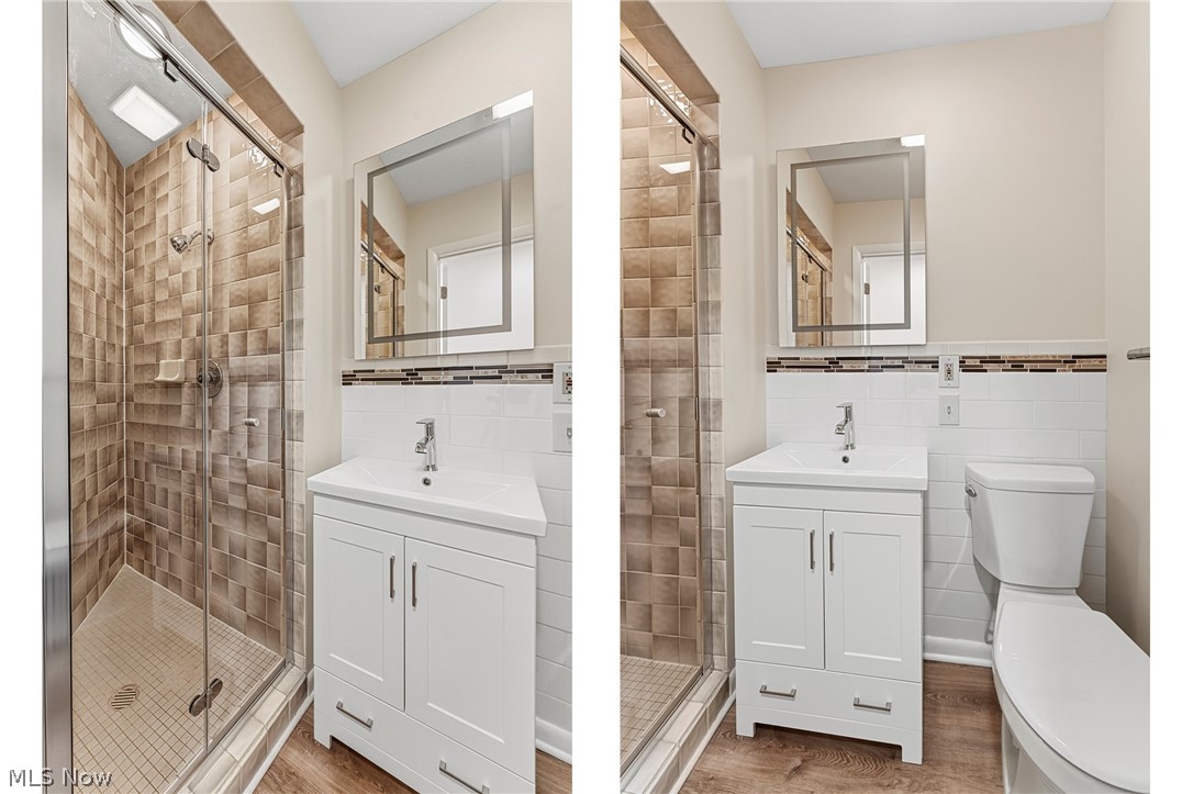 13011 West Lake Road Vermilion, OH 44089 - Photo 9 of 29 Bathroom featuring a glass-enclosed shower with textured tile surround, a white vanity with integrated sink, wood-finish flooring, a contemporary mirror, and a toilet
