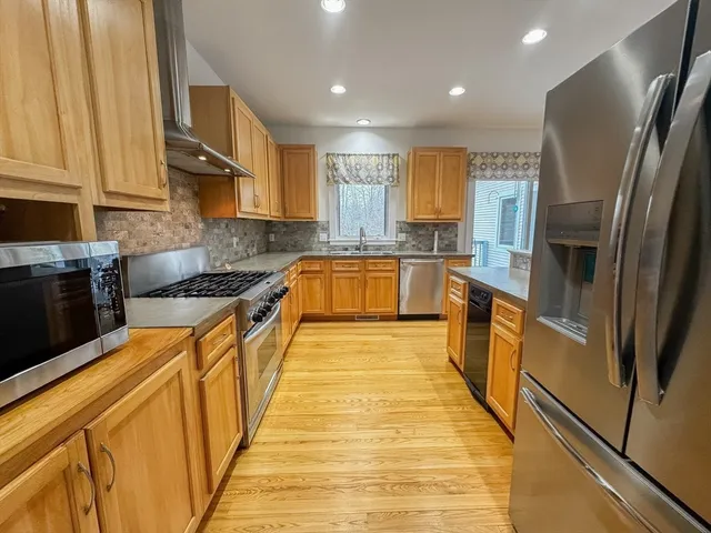 a large kitchen with stainless steel appliances granite countertop a refrigerator a sink dishwasher a stove and white countertops with wooden floor