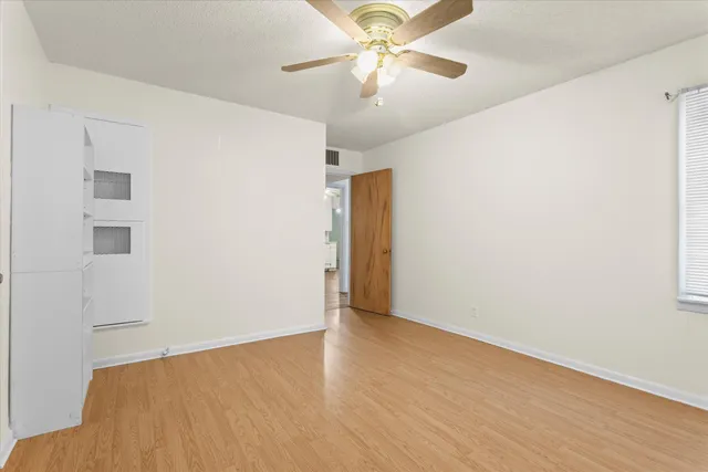an empty room with wooden floor fan and windows