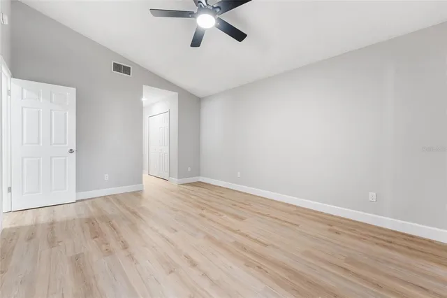 a view of an empty room with wooden floor and a ceiling fan