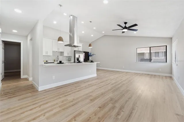 a view of an empty room and kitchen with wooden floor