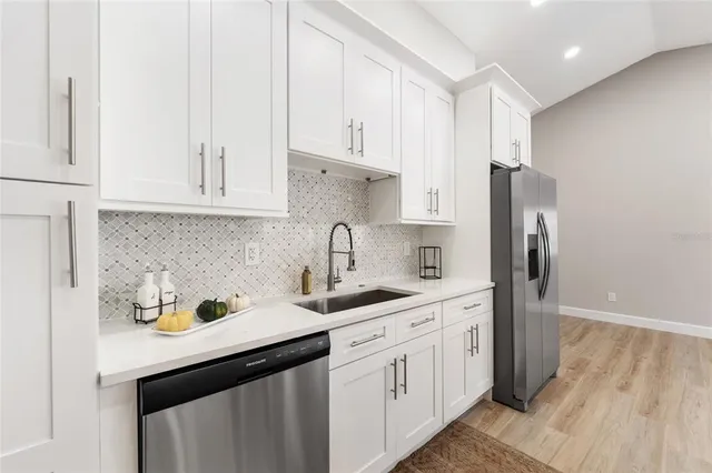 a kitchen with stainless steel appliances granite countertop a sink a refrigerator and white cabinets