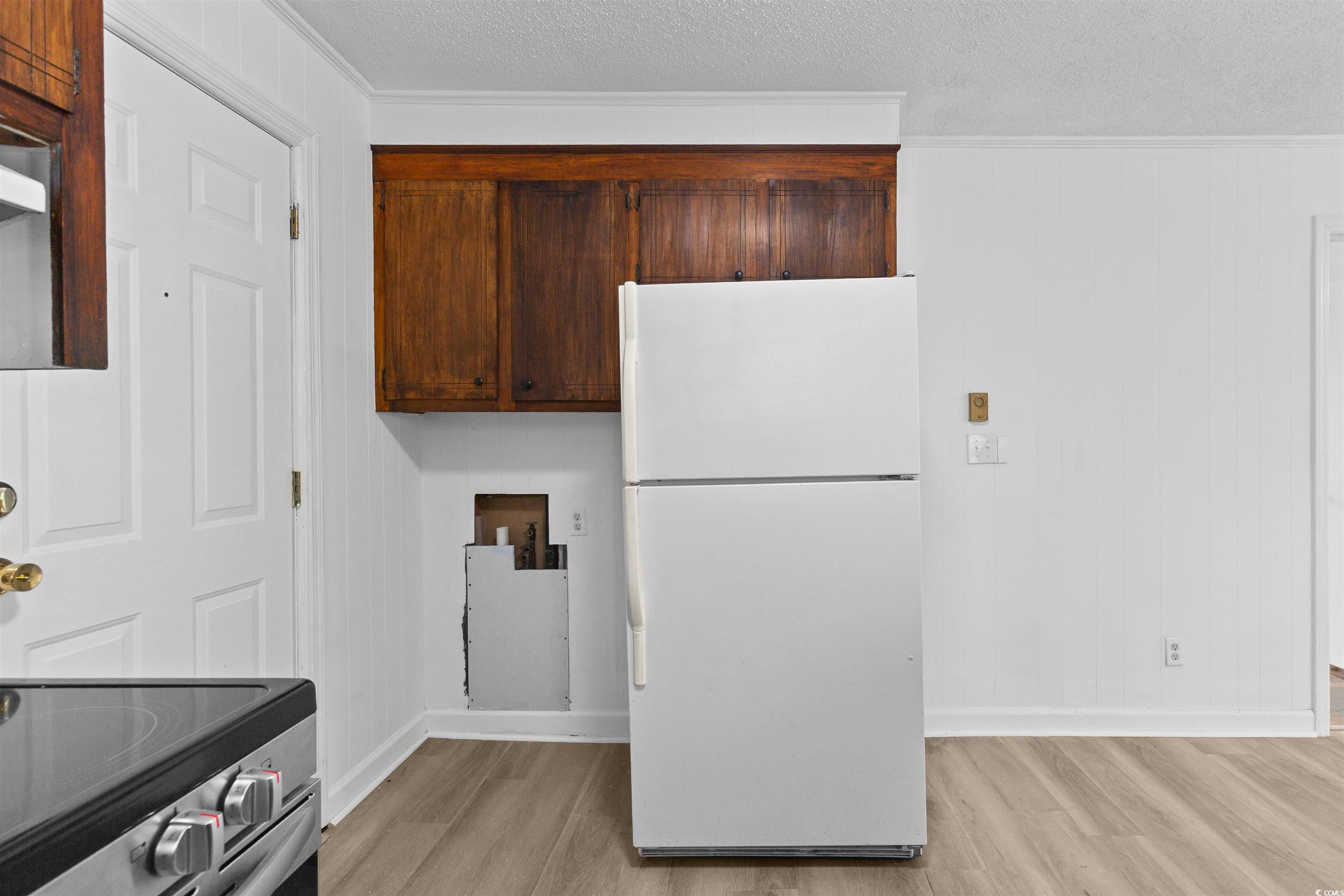 139 State Rd S-22-496 Andrews, SC 29510 - Photo 7 of 20 Kitchen featuring freestanding refrigerator, light wood-type flooring, a textured ceiling, wood walls, and dark brown cabinets