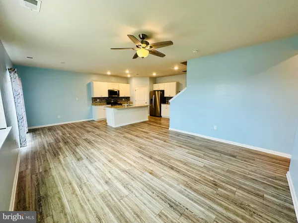 an empty room with kitchen view and a ceiling fan