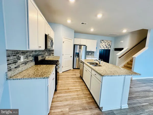 a large white kitchen with granite countertop a sink and dishwasher a stove with wooden floor