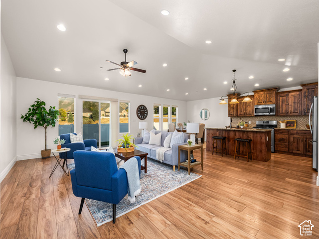 Vaulted ceilings with recessed lighting, wood-finish flooring, sliding glass patio doors, a kitchen island with seating, and wood cabinetry with stainless steel appliances