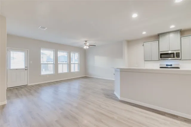 a view of an empty room with kitchen and window