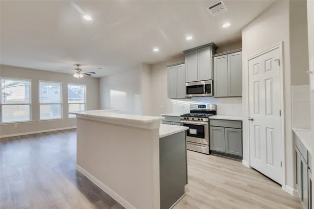 a kitchen with stainless steel appliances granite countertop a stove top oven a sink dishwasher a refrigerator and a microwave oven with wooden floor