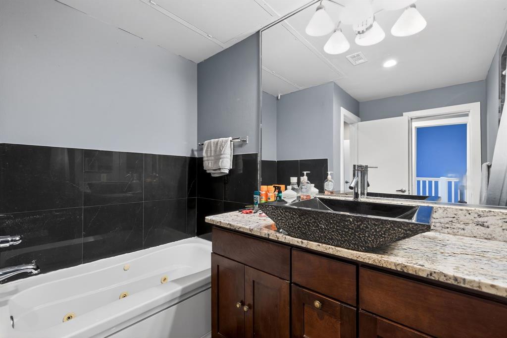 5055 Addison Circle, Unit 713 Addison, TX 75001 - Photo 21 of 40 Bathroom featuring a jetted tub, black tile wainscoting, a vessel sink, a granite countertop, and wood-finish cabinetry