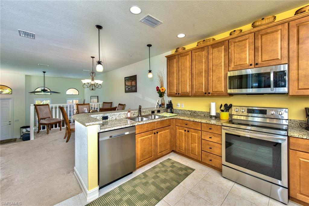 9102 Capistrano Street South, Unit 7209 Naples, FL 34113 - Photo 8 of 25 a kitchen with stainless steel appliances granite countertop a stove top oven a sink dishwasher a dining table and chairs with wooden floor