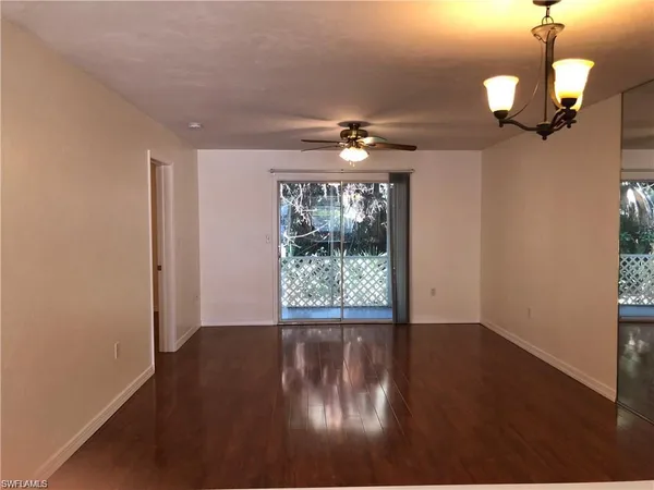 an empty room with wooden floor chandelier fan and windows