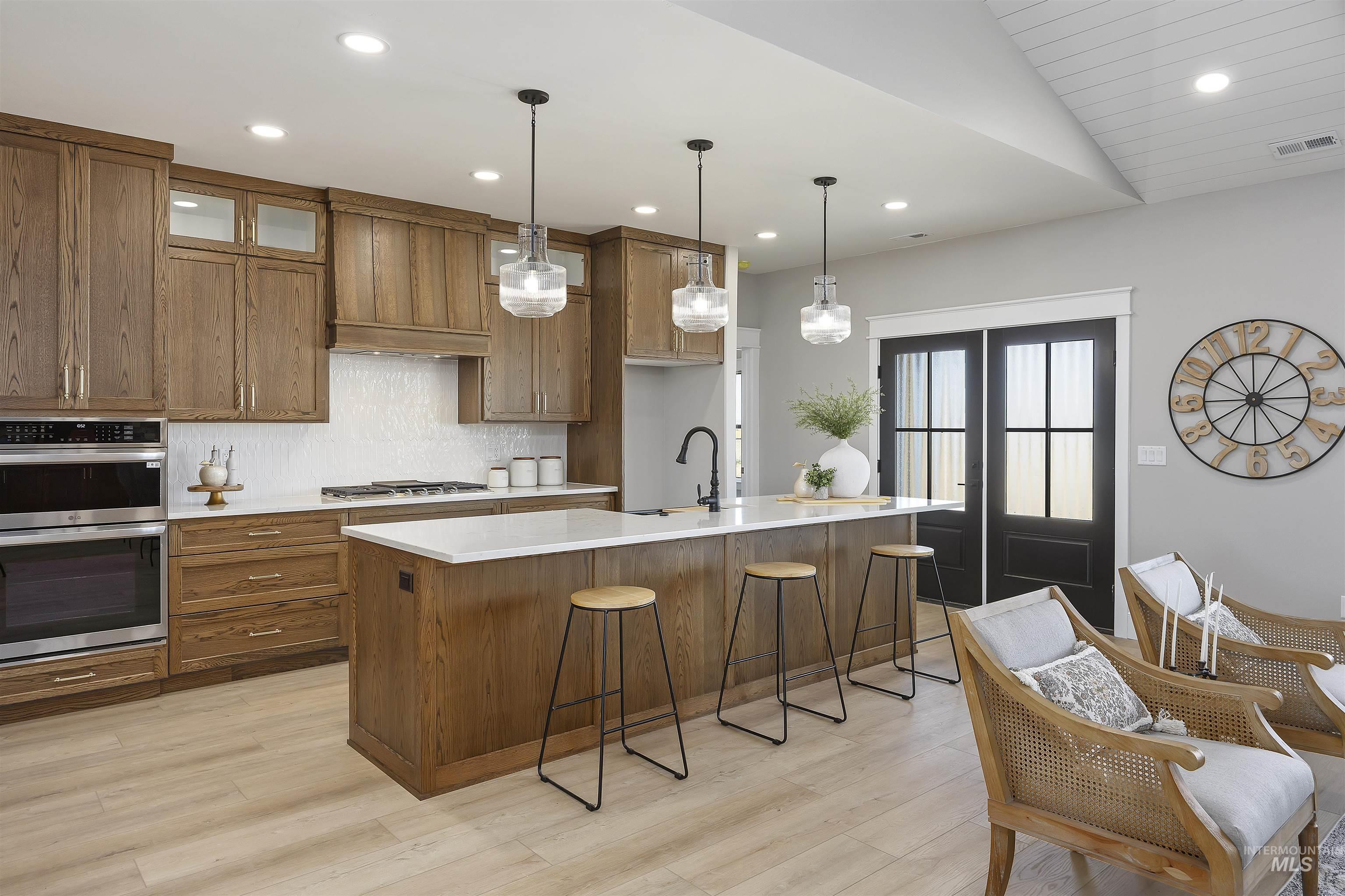 378 West 100 South Rupert, ID 83350 - Photo 11 of 50 Gourmet kitchen featuring wood-finish cabinetry, stainless steel double ovens, a white subway tile backsplash, and a large center island with a white countertop and pendant lighting