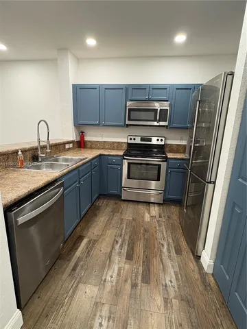 a kitchen with stainless steel appliances granite countertop a refrigerator a sink a stove top oven and wooden floor