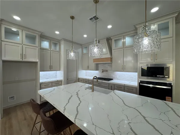 a large kitchen with kitchen island a stove a sink a refrigerator white cabinets and wooden floor