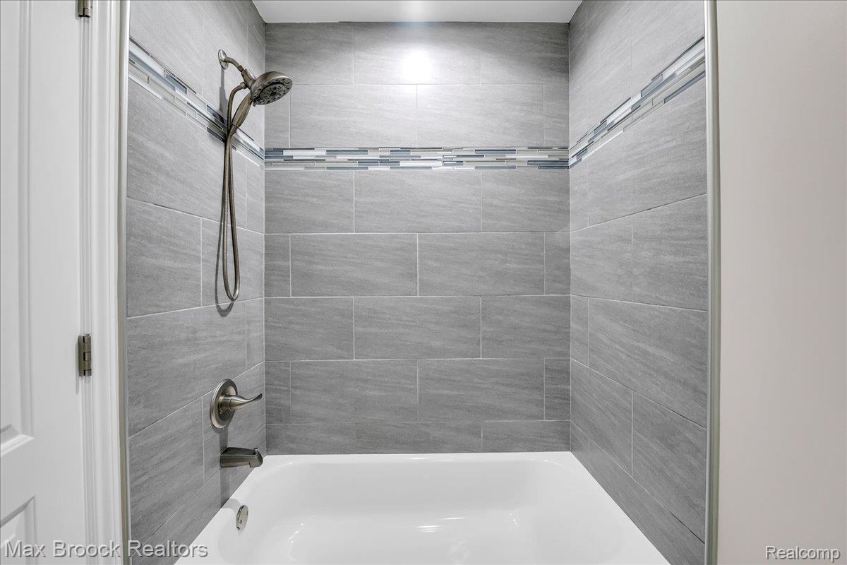 1126 Queensboro Drive Rochester, MI 48307 - Photo 35 of 66 White bathtub with bronze-finish fixtures, light gray tile surround, and an accent tile band
