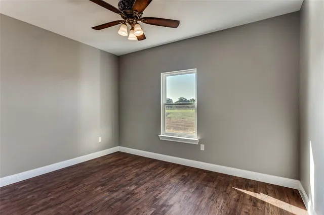 an empty room with wooden floor chandelier fan and windows